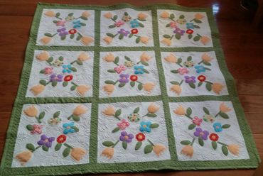 Handmade quilt with floral appliqué on wooden floor